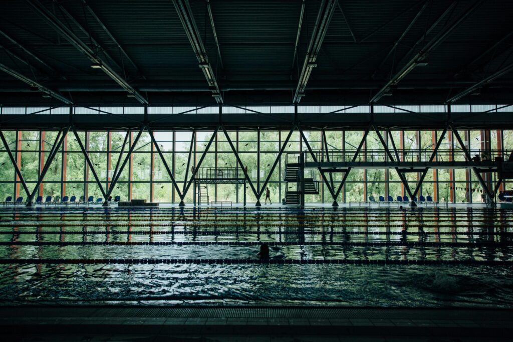Unrecognizable sportsman silhouette strolling between decorative wall and swimming pool with rippled water and floating markers